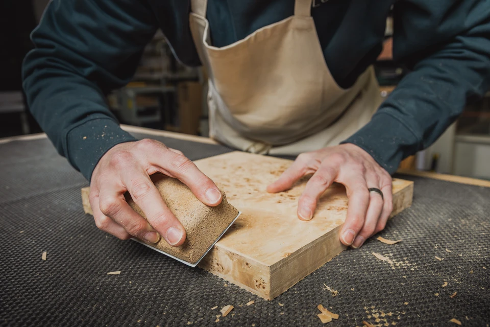 Un artisan applique un produit de finition sur un parquet en bois avec un pinceau large
